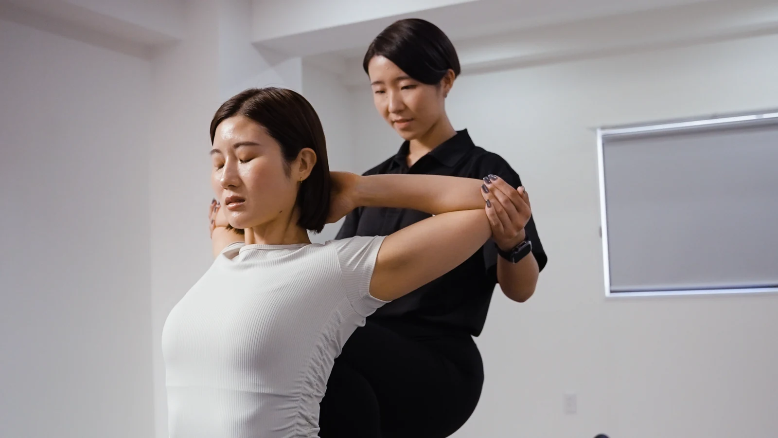 女性トレーナーが肩と胸のストレッチをサポートする施術イメージ